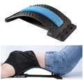 Le Fashiongirl Pro Back Stretcher, présenté seul avec un coussin bleu, est également présenté par une personne vêtue d'un t-shirt noir et d'un jean bleu qui l'utilise pour soutenir ses lombaires et corriger sa posture.