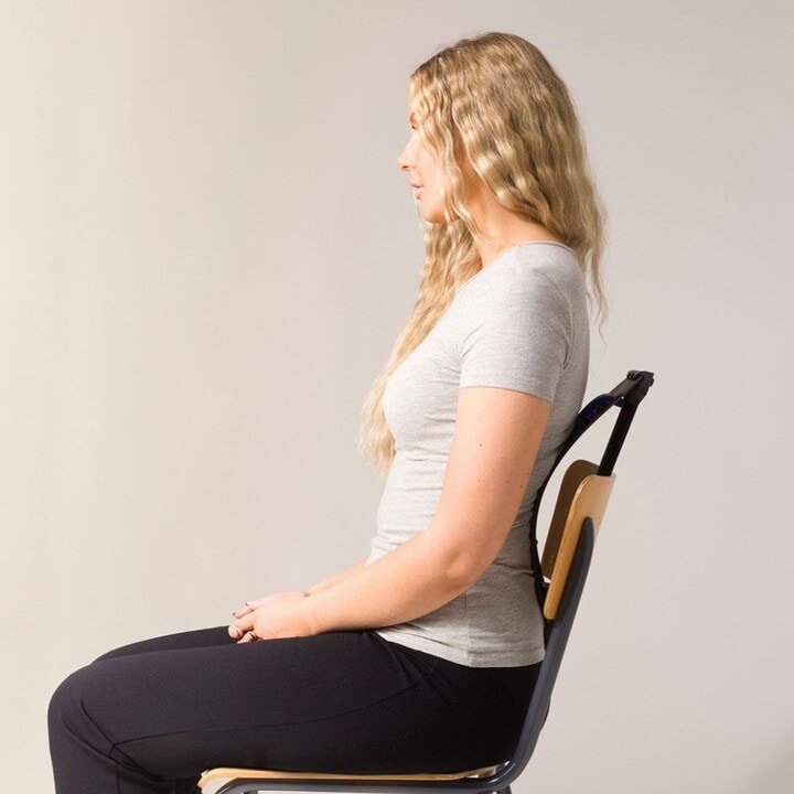Une femme aux longs cheveux blonds est assise bien droite sur une chaise, utilisant le Fashiongirl Pro Back Stretcher pour corriger sa posture et soulager ses douleurs, démontrant son efficacité sur un fond clair et uni.