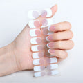 Une main aux ongles manucurés tient des autocollants pour ongles UNIQ Semi Cured Gel Nail Stickers / Self-adhesive nail polish - Classic French (JK-331), avec un motif chic en demi-lune blanc et rose pâle qui s'harmonise parfaitement avec les ongles.