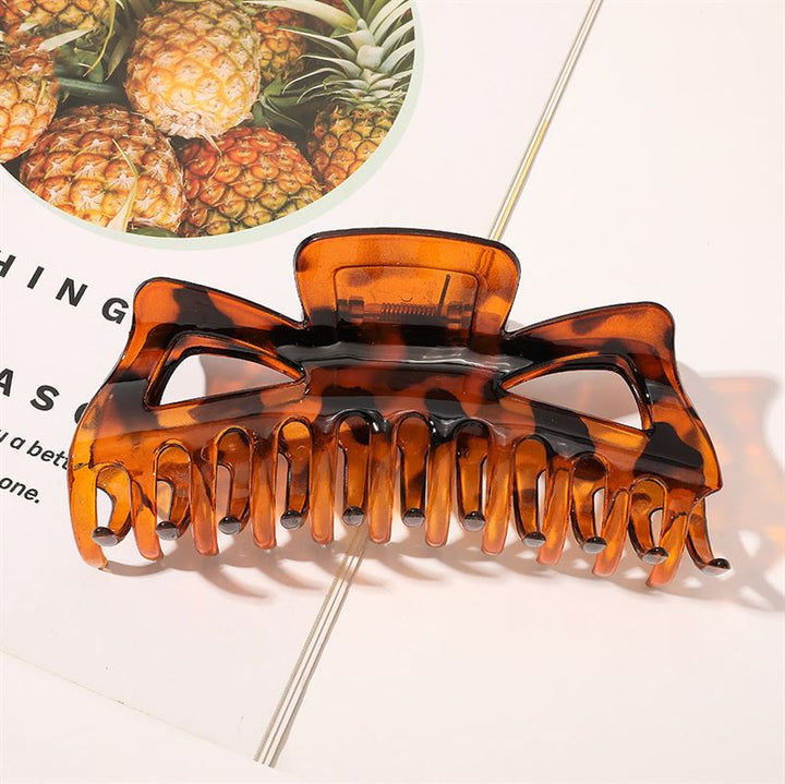 The SOHO Astrid Hair Claw - Tortoise by SOHO, designed for thick hair, sits on a magazine page with pineapple images, casting a distinct shadow.