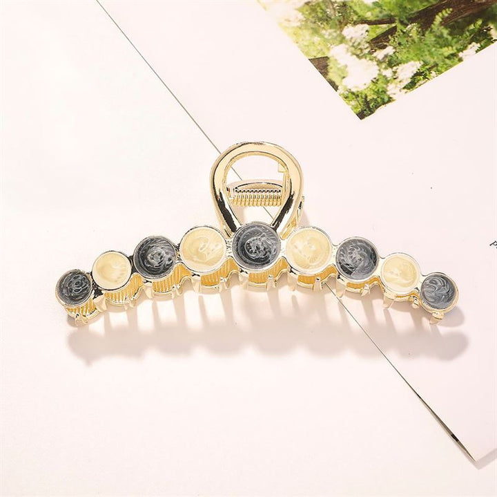 The SOHO Becca Hair Claw - Midnight by SOHO features gold metal with black and cream accents, shown on a white surface near floral paper—ideal for securing messy buns or adding style to your hair accessories collection.