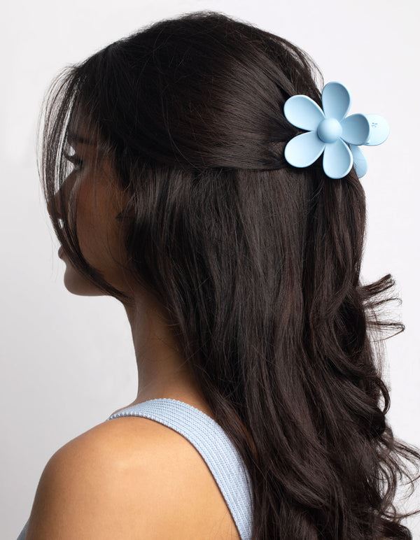 A woman with long, wavy dark hair wears the SOHO Bloom Hair Claw in Light Blue by SOHO on the side of her head. She faces left in a ribbed top against a plain white background.