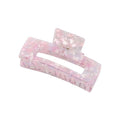 La pince à cheveux SOHO Clara - Lavender Pink est une grande pince rectangulaire en acrylique rose et blanc marbré, avec une finition brillante et translucide et une charnière à ressort, idéale comme accessoire XL pour les cheveux épais.