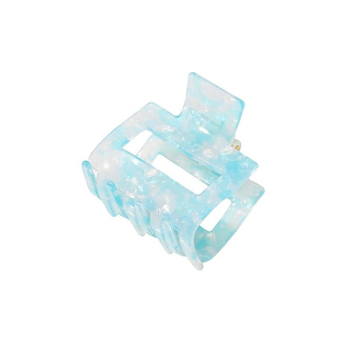 The SOHO Ema Hair Claw in Crystal Blue features a semi-transparent, marbled light blue design with a rectangular cutout and interlocking teeth—ideal for adding chic, effortless hold to any elegant hairstyle.