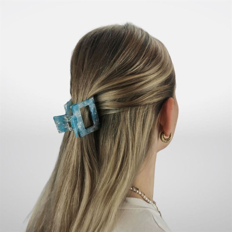 A person with long, blonde hair is seen from behind, the top section secured with the SOHO Ema Hair Claw in Crystal Blue. Gold hoop earrings and a beaded necklace complete their stylish look, showcasing this chic SOHO accessory.