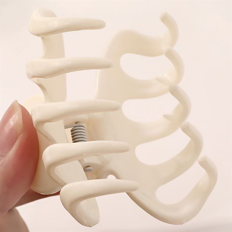 A close-up of a hand holding the SOHO Esta Hair Claw in White by SOHO, featuring wide, curved prongs and a metal spring hinge for extra grip—perfect for hairstyling.