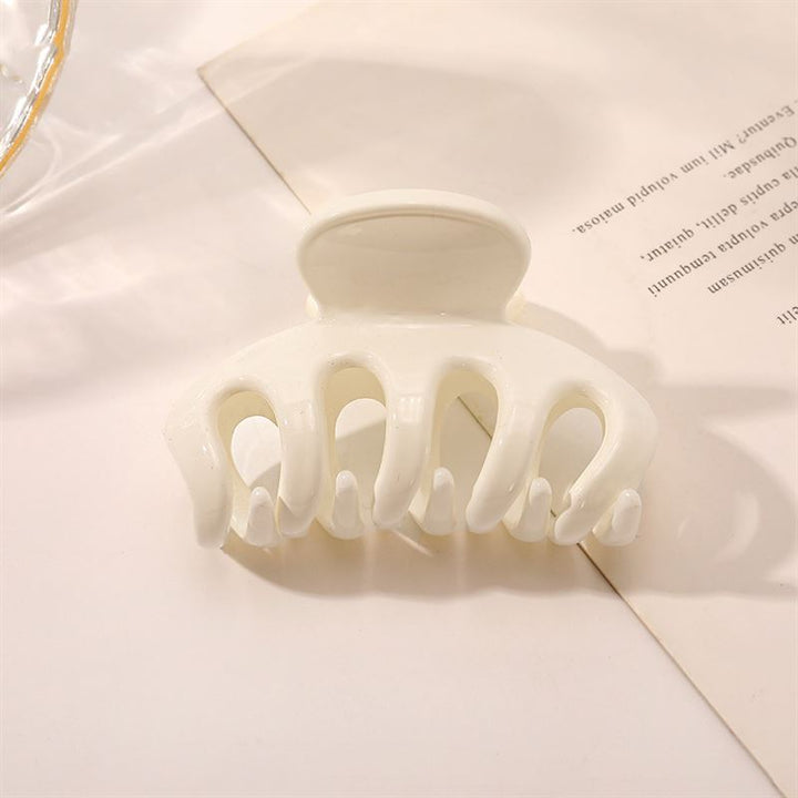 The SOHO Esta Hair Claw - White by SOHO, designed for extra grip, rests on a slightly angled piece of paper with printed text on a light-colored surface.