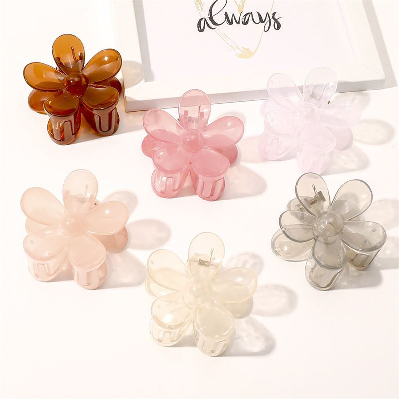 La pince à cheveux SOHO Fiore - Charm Pink de SOHO est présentée sur une surface blanche parmi d'autres pinces colorées, avec en arrière-plan une illustration encadrée représentant le mot « always ».