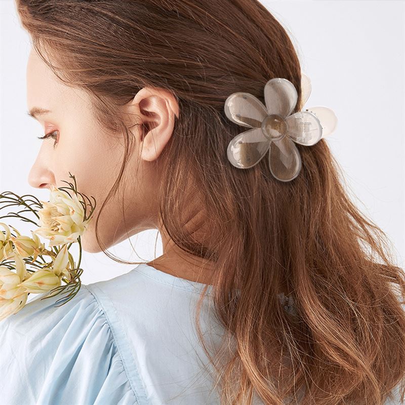 Une femme aux longs cheveux bruns porte la barrette SOHO Fiore Hair Claw en rose charme, tournée sur le côté, vêtue d'un haut bleu clair et tenant un bouquet de fleurs jaune clair.