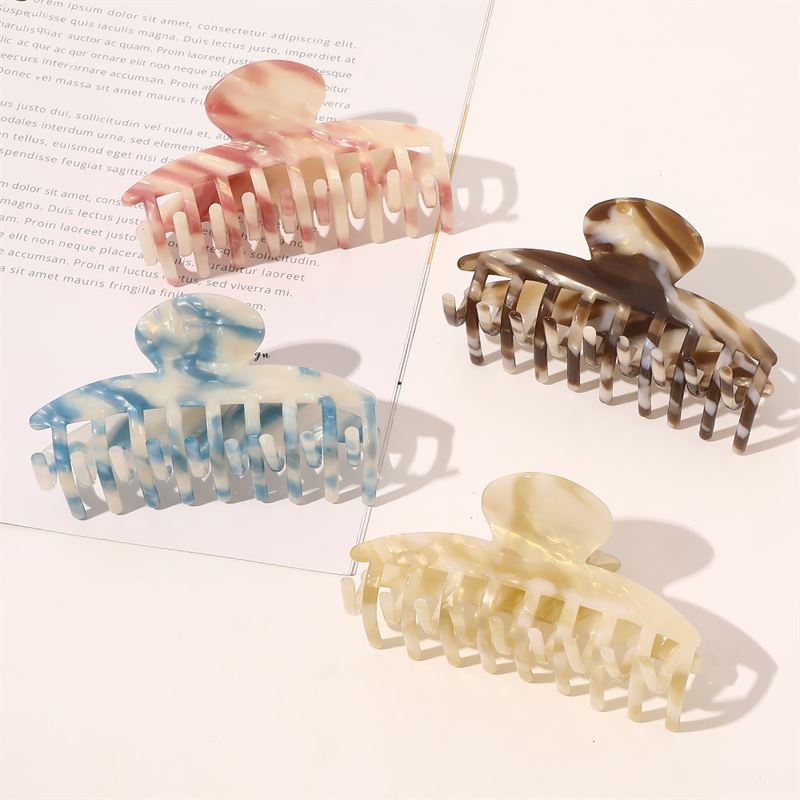 The SOHO Gaja Hair Claw in Brown Marble is displayed on a white surface alongside pink, blue, and beige marbled claws, with a partially visible printed paper nearby.