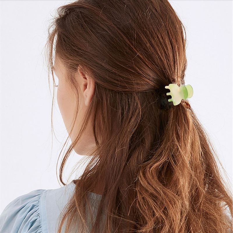 A person with long, wavy brown hair, seen from behind in a light blue top, secures their hair in a loose half-up style using the SOHO Hara Mini Hair Claw - Light Tortoise by SOHO.