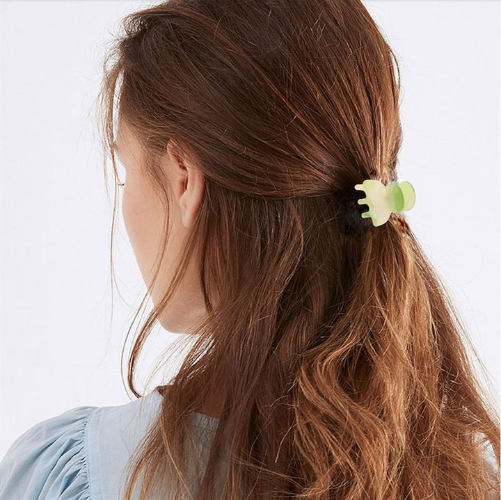 A woman with long, wavy brown hair is seen from behind, her hair partially pulled back with the SOHO Hara Mini Hair Claw in Periwinkle. She wears a light blue blouse for a soft, elegant look.