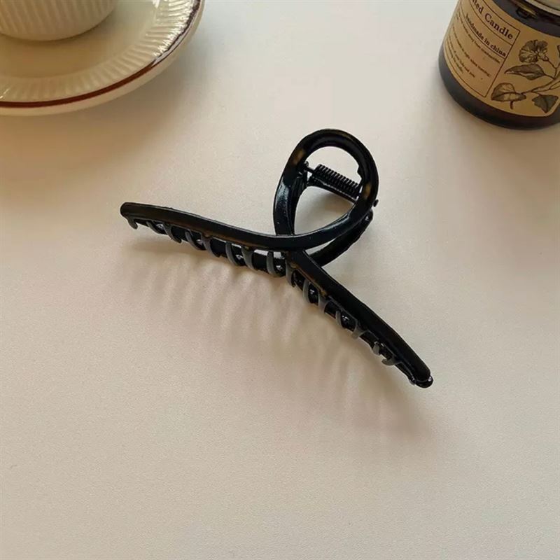 The SOHO Iva Metal Hair Claw in black by SOHO is displayed on a white surface beside a teacup, saucer, and brown glass candle jar—ideal for securing messy buns or adding chic style to your hair.