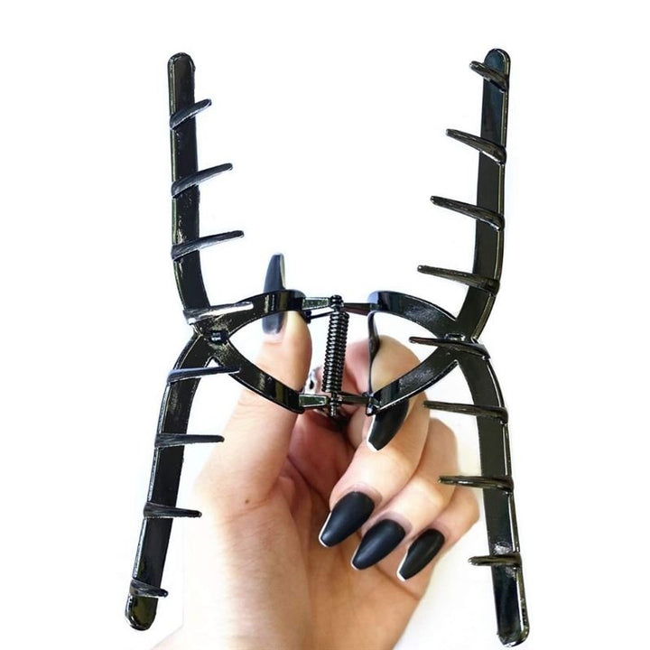 A hand with long, matte black nails holds the SOHO Iva Metal Hair Claw in Black, a large accessory by SOHO featuring widely spaced teeth—perfect for securing a messy bun—against a white background.