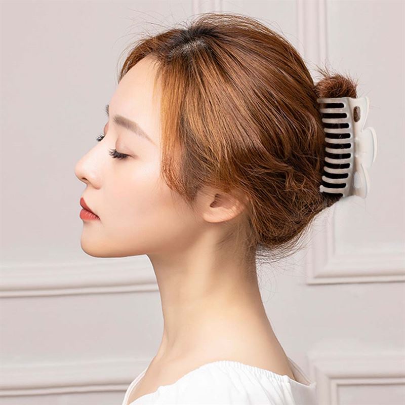 A woman with light brown hair in a bun, secured by the SOHO Jelly Hair Claw - Beige from SOHO, is shown in profile against a light wall. She wears a white top and looks calm; this strong-grip accessory suits all hair types.