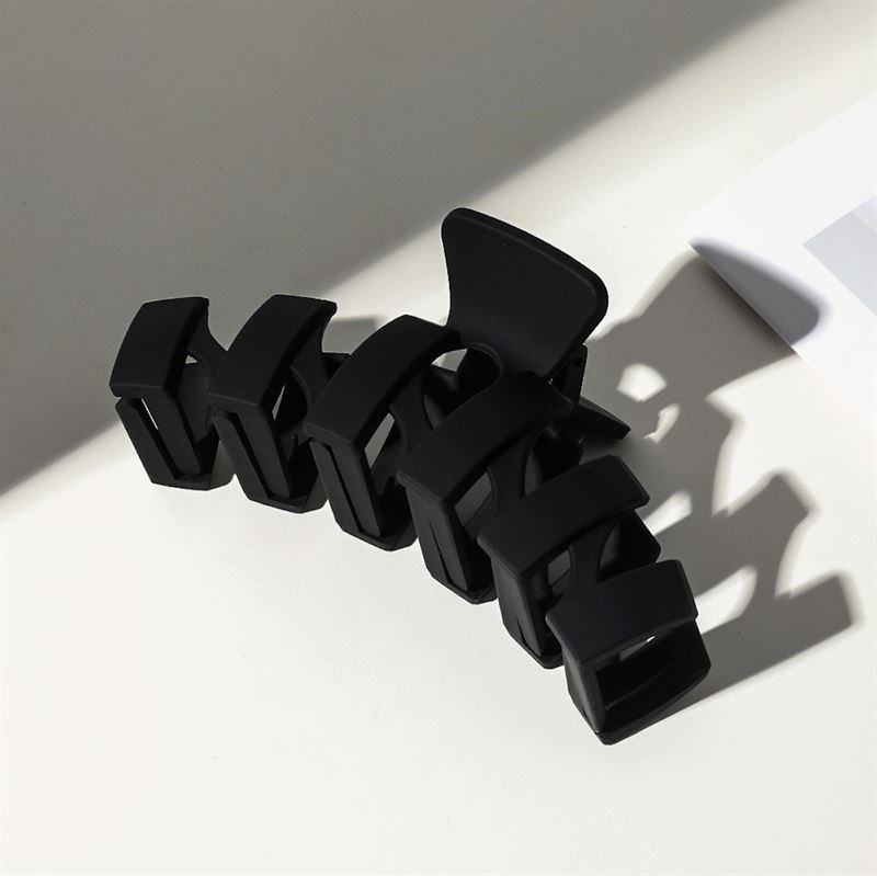 The SOHO Just Hair Claw - Black by SOHO features a large matte finish and wide rectangular prongs, casting a sleek shadow on a white surface. This chic accessory brings modern style to any look.