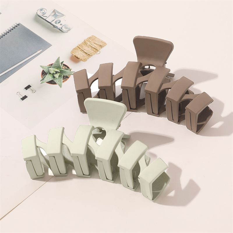 The SOHO Just Hair Claw in brown by SOHO rests elegantly on an open magazine with stationery and a geometric paper star, softly lit to highlight its matte finish and stylish design against a pale background.