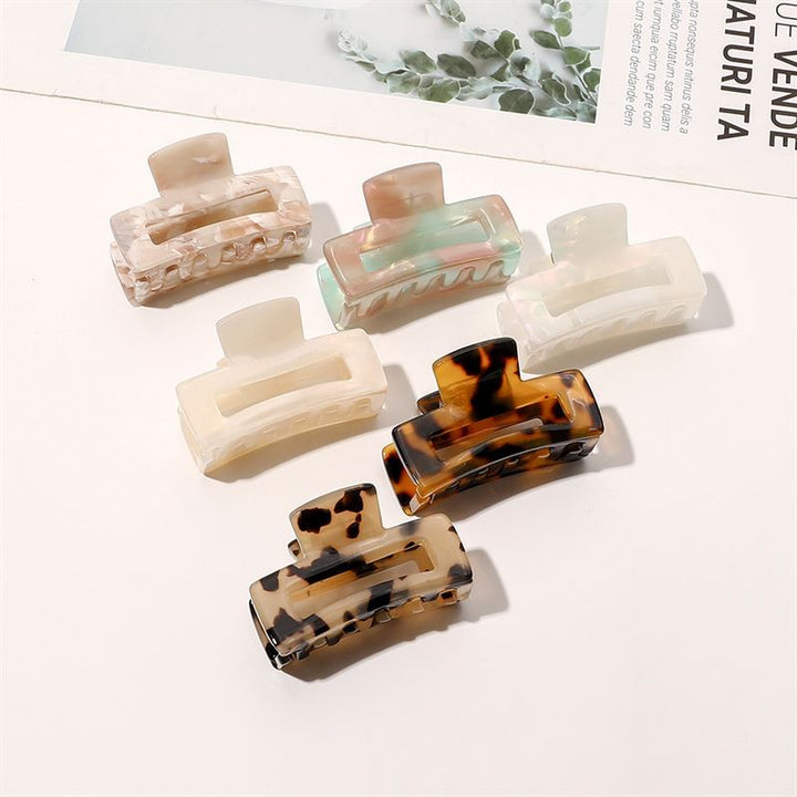 The SOHO Leia Mini Hair Claw - Pearl by SOHO rests on a white surface beside a magazine and leafy branch, ready to add effortless style to your hair.