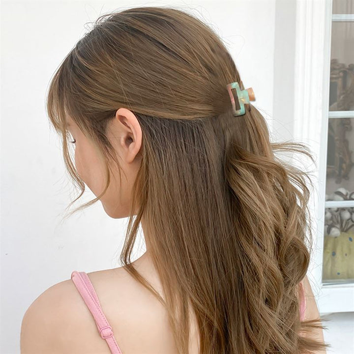 A woman with long, light brown wavy hair styled half up using the SOHO Leia Mini Hair Claw in Pearl, wearing a pink sleeveless top, is seen from behind and slightly to the side against a light background.