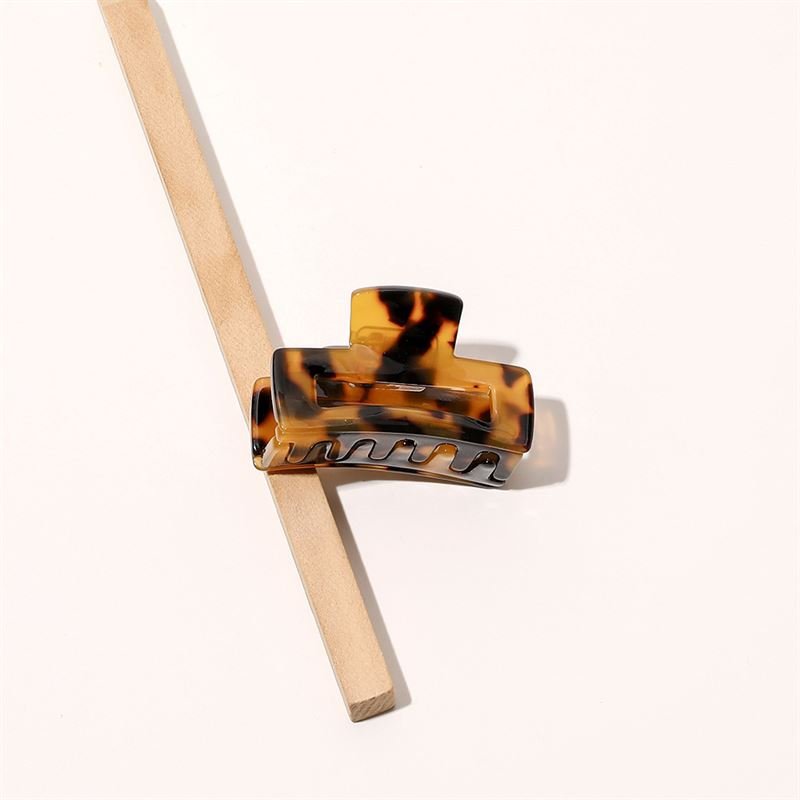 The SOHO Leia Mini Hair Claw - Tortoise by SOHO rests on a diagonally placed wooden stick against a light background, making it perfect for effortless hairstyling.