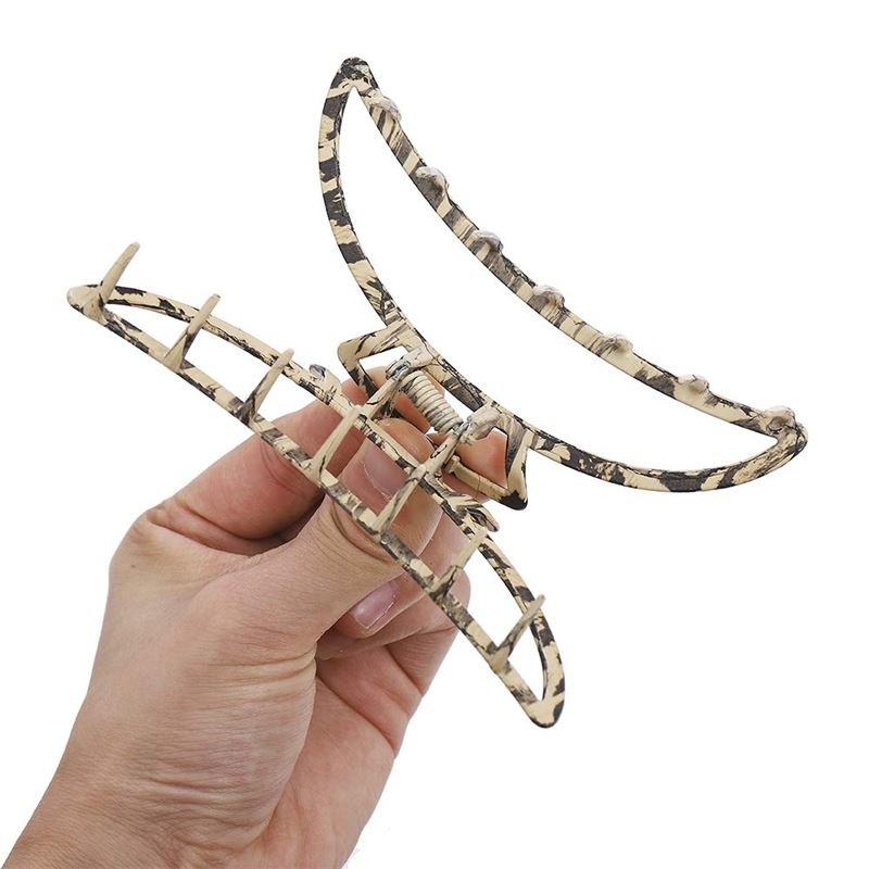 A hand holds the SOHO Leopard Metal Barette Hair Claw, a stylish beige and black accessory by SOHO, shown against a plain white background.