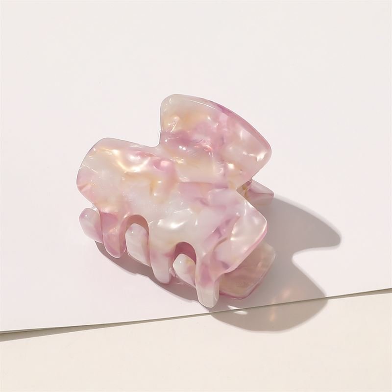 The SOHO Loa Mini Hair Claw in Blush, featuring a pastel pink marble look and glossy finish, rests on a white surface and casts a soft shadow in the sunlight.