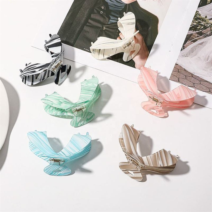 The SOHO Malou Hair Claw - Green by SOHO is displayed on a white surface beside an open fashion magazine, featuring a butterfly shape and stylish pastel and striped design.