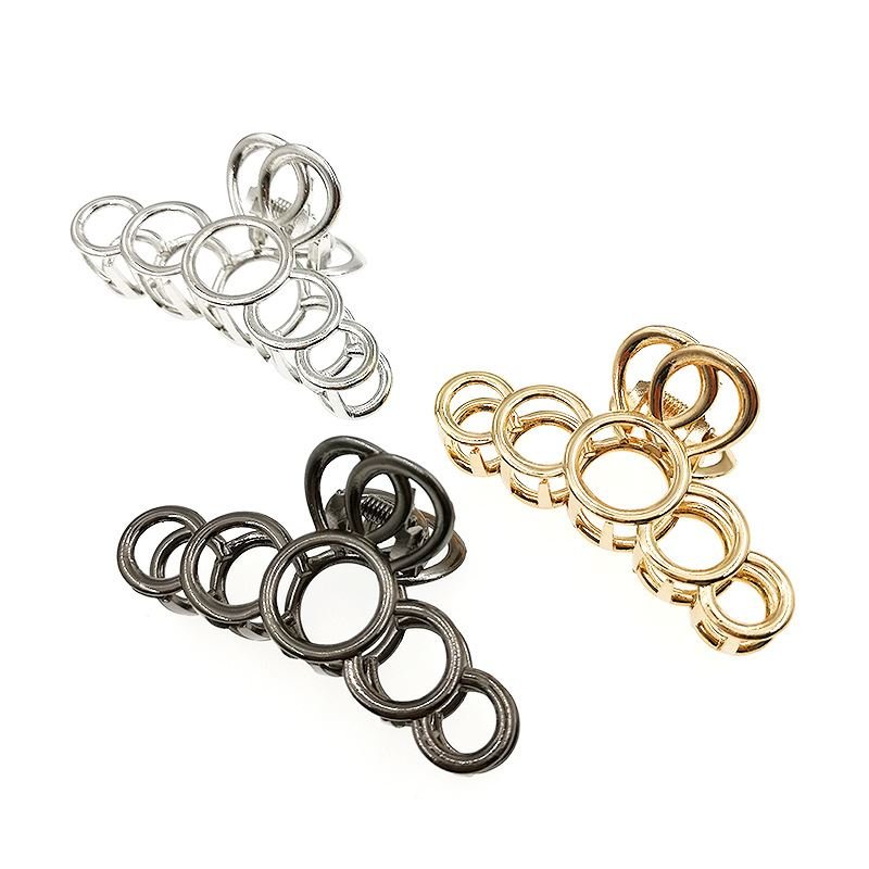 La pince à cheveux métallique SOHO en argent de SOHO est composée d'anneaux métalliques entrelacés de différentes tailles, conçus pour maintenir les cheveux épais avec élégance et style, et est présentée sur un fond blanc.