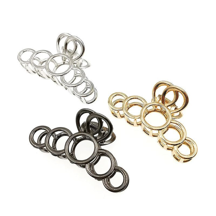 La pince à cheveux métallique SOHO en argent de SOHO est composée d'anneaux métalliques entrelacés de différentes tailles, conçus pour maintenir les cheveux épais avec élégance et style, et est présentée sur un fond blanc.
