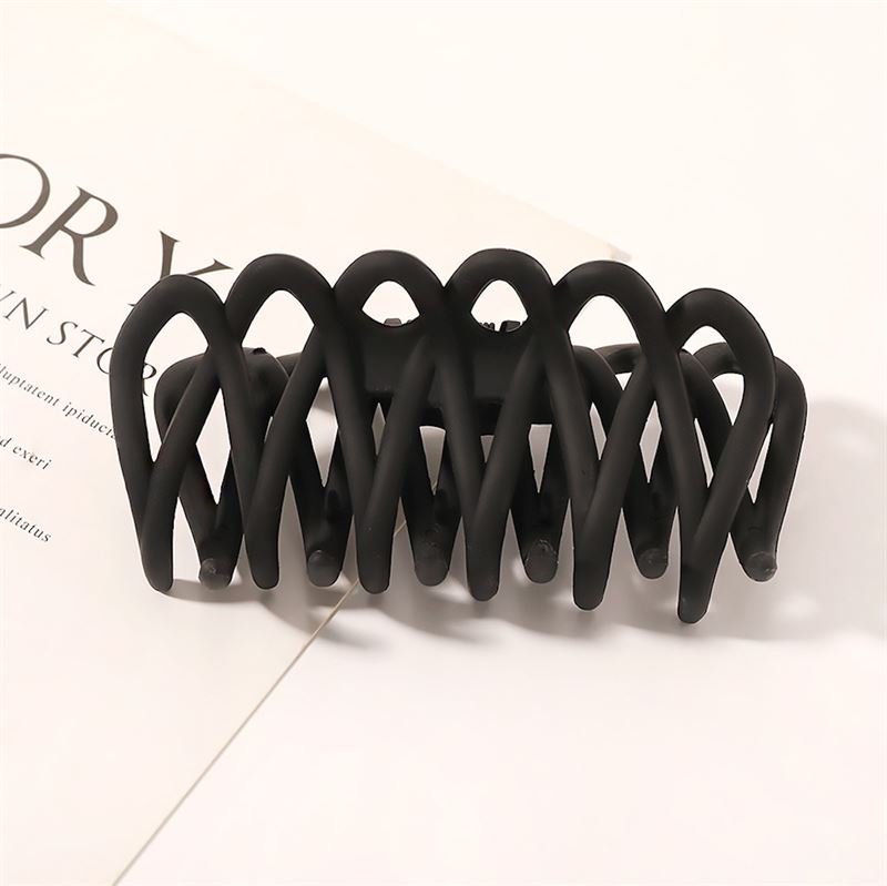 The SOHO Olive Hair Claw - Black by SOHO features a matte finish and interlocking curved prongs for a gentle grip, perfect for securing all hair types—shown resting on an open magazine with visible text on a white background.