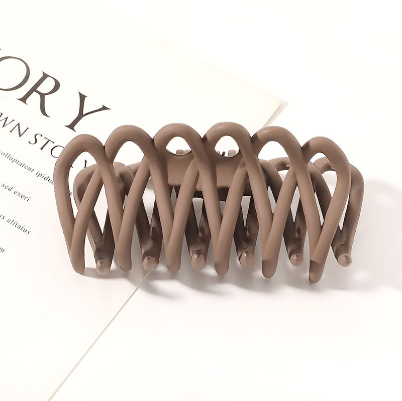 The SOHO Olive Hair Claw - Brown by SOHO features a matte, interwoven curved design and gentle grip, shown resting on a white surface near printed text—ideal for securing all hair types.