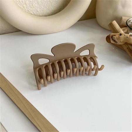 The SOHO Zara Hair Claw - Caramel by SOHO, a large matte beige claw with wide teeth, rests on a white and wooden surface amid neutral decor—an elegant, practical hair accessory perfect for daily use.