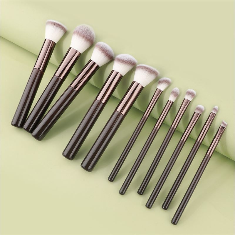 The Technique PRO Chocolate Bronze Makeup Brush Set features 11 professional brushes with dark handles and white-tipped bristles, neatly arranged on a light green background for all your makeup application needs.