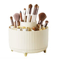 Le range-maquillage rotatif UNIQ en blanc crème présente un design à plusieurs niveaux et nervuré avec des compartiments et des pieds dorés, offrant un rangement et une organisation faciles pour les pinceaux, les rouges à lèvres, les crayons et les produits de beauté.